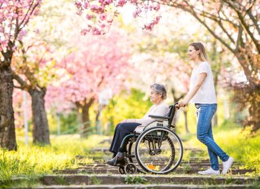 Elderly grandmother in wheelchair with granddaughter in spring nature.